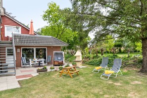 Un jardin avec une terrasse, une table, des chaises, une petite maison de jeu et deux fauteuils de jardin.