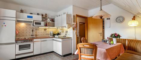 A kitchen with white cabinets, a microwave, an oven, and a dining area with a table and chairs.