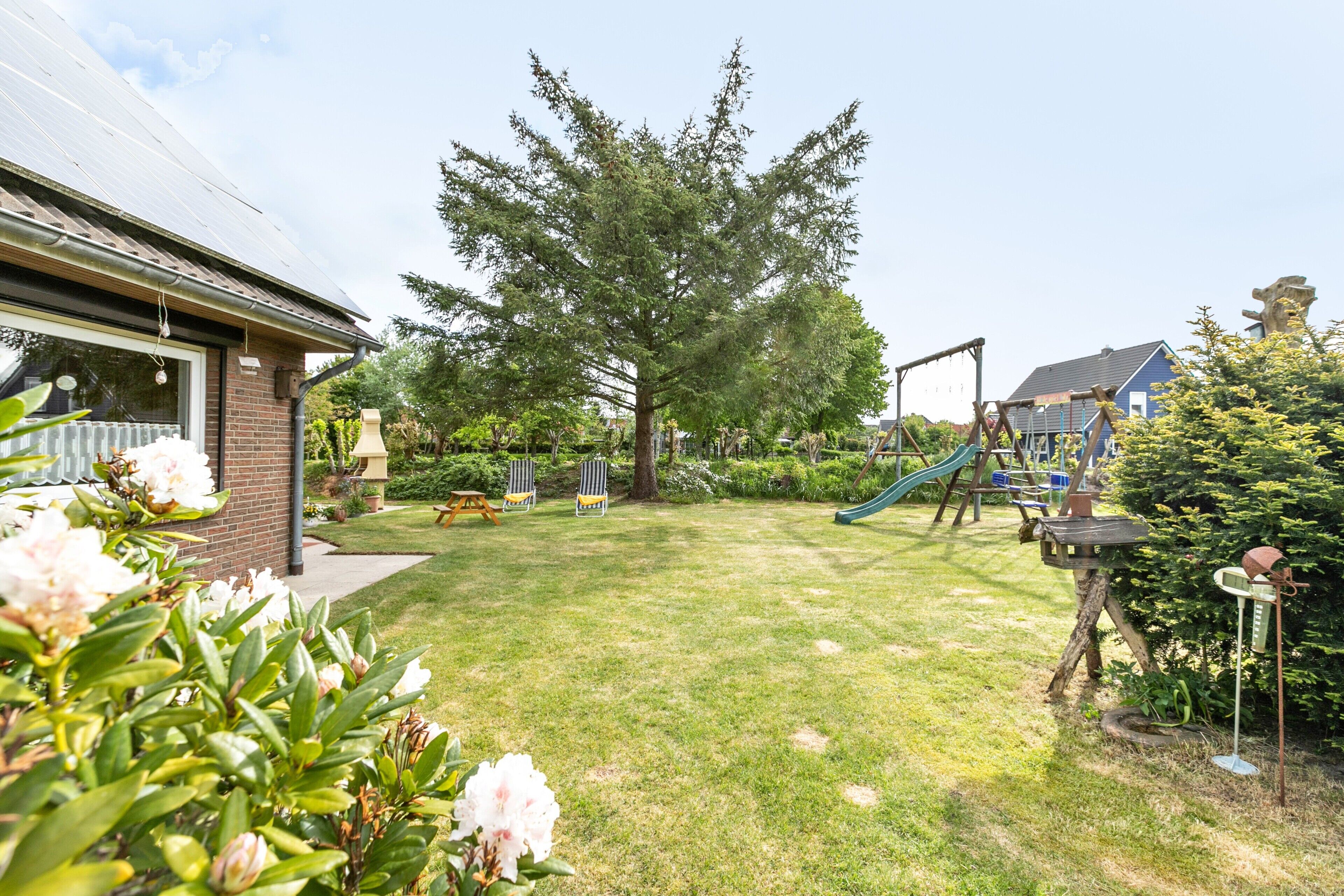 A residential backyard with a grassy lawn, a large tree, a swing set, and a playhouse.
