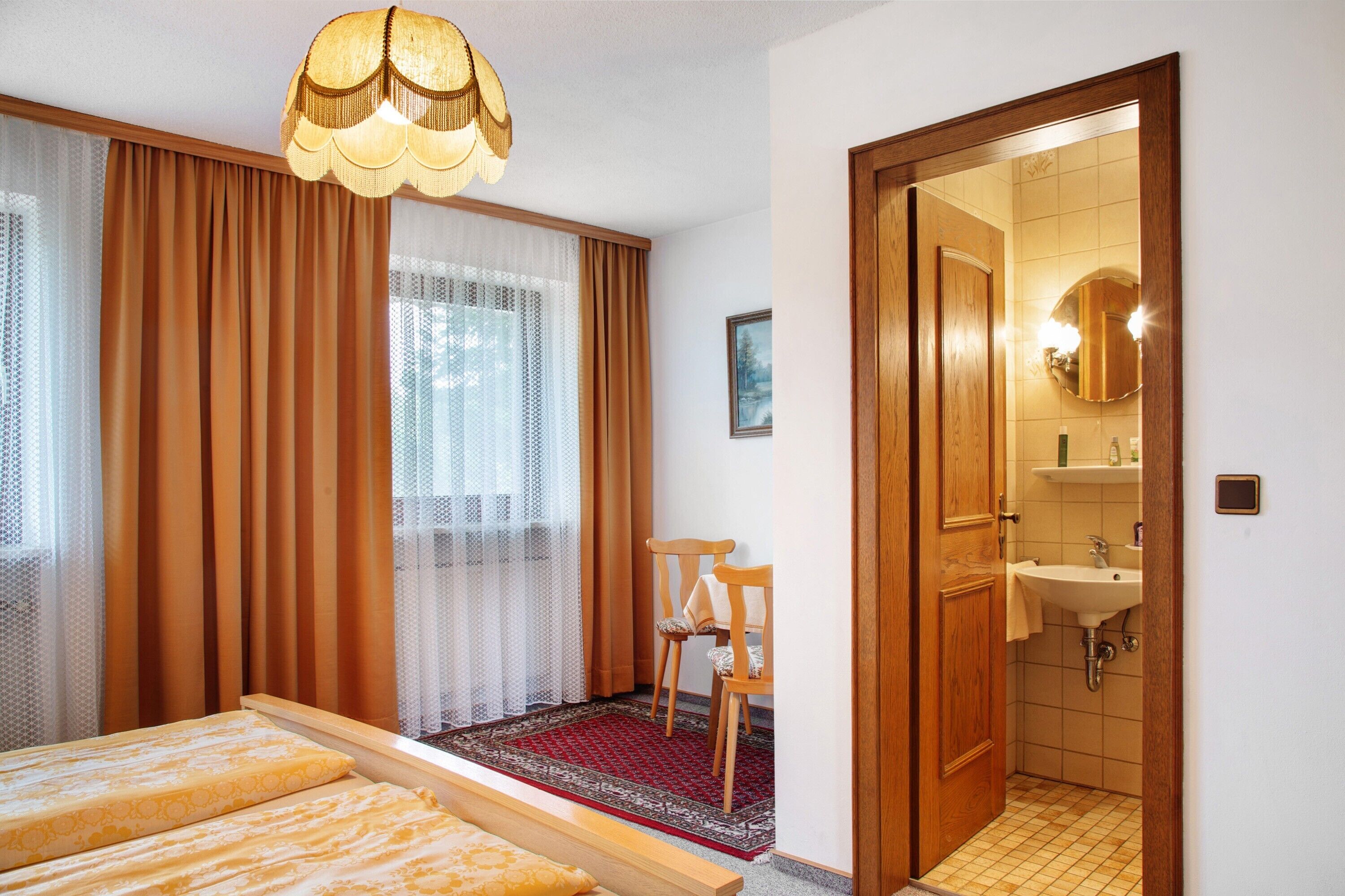 A hotel room with a bed, a chair, a bathroom with a sink, and a mirror.