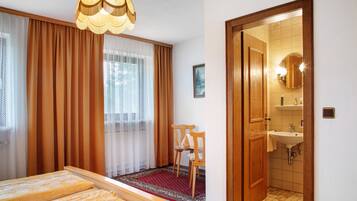 Una habitación de hotel con una cama, una silla, un baño con lavamanos y un espejo.