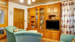 A living room with wooden cabinets, a television, and two green armchairs.
