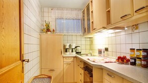 A kitchen with wooden cabinets, a tiled backsplash, a window with a lace curtain, and various kitchen appliances.
