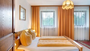 A hotel room with a bed, a wooden headboard, a hanging light fixture, and sheer curtains.