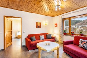 Una habitación con techo de madera, un sofá rojo, una mesa blanca y una ventana con vista a un puente.
