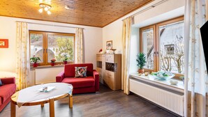 Une pièce chaleureuse avec un plafond en bois, un canapé rouge, un meuble en bois et une fenêtre avec des rideaux.