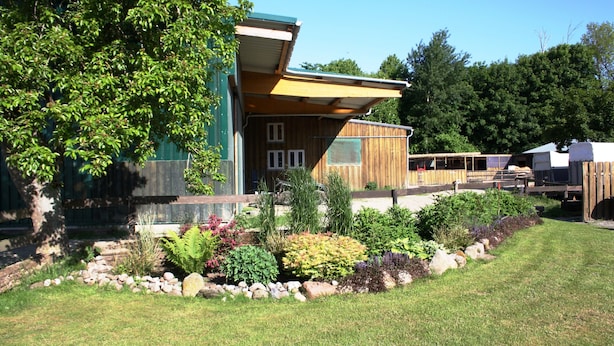 Uma casa moderna com um amplo jardim, um deck de madeira e uma área externa coberta.