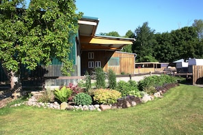 A modern house with a large garden, a wooden deck, and a covered outdoor area. - Apartment '2002' with Private Terrace, Garden, and Wi-Fi (Wesselburenerkoog)