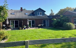 A two-story house with a sloped roof, a patio with outdoor furniture, and a well-maintained lawn. - Apartment '2002' with Private Terrace, Garden, and Wi-Fi (Wesselburenerkoog)