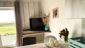 A room with a large window, a flat-screen TV, a teal vase with dried plants, a tray with eggs, and a teal sideboard.