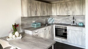 A modern kitchen with light wood cabinetry, a central island, a built-in oven, and a small sink.