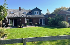 A two-story house with a sloped roof, a patio with outdoor furniture, and a well-maintained lawn.