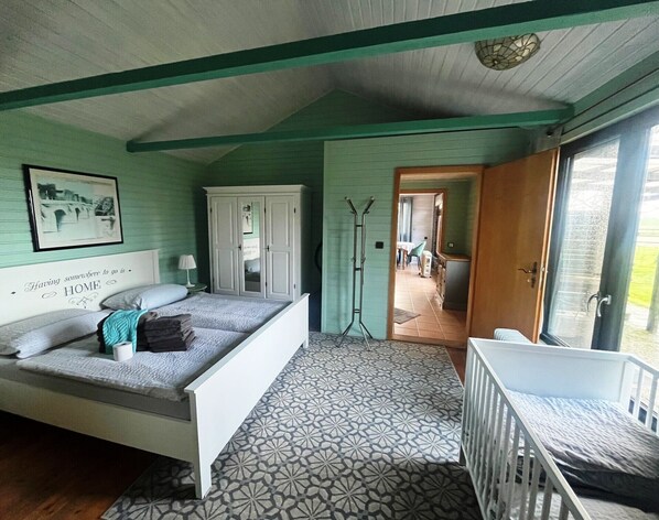 A bedroom with a bed, a crib, a wardrobe, a mirror, and a door leading to another room.