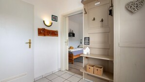 A hallway with a door, a wall-mounted light, a shelf with a sign, and a bed in the background.