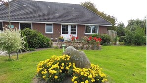 A house with a brick exterior, a tiled roof, and a well-maintained lawn with yellow flowers.