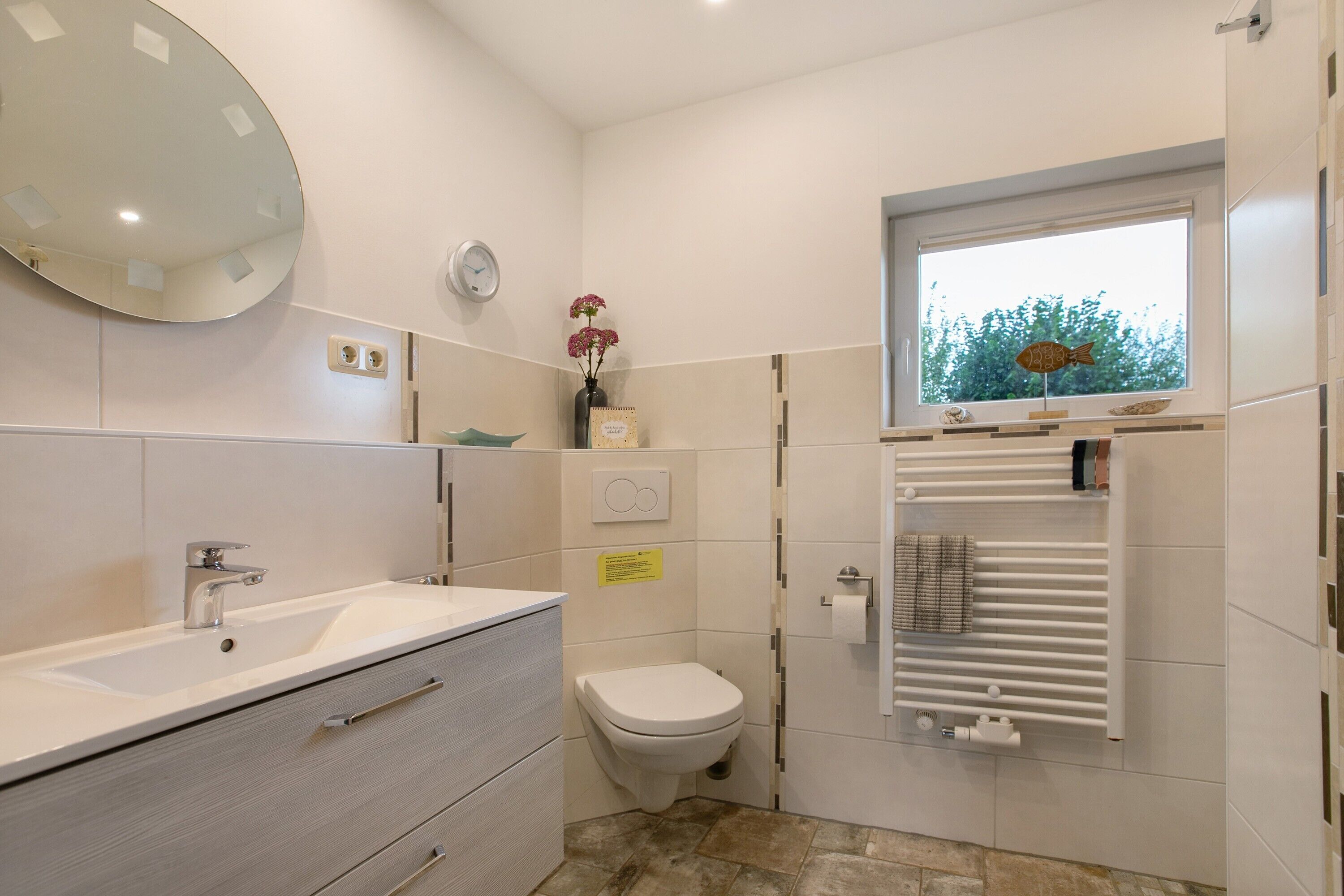 A modern bathroom with a sink, toilet, mirror, and window.