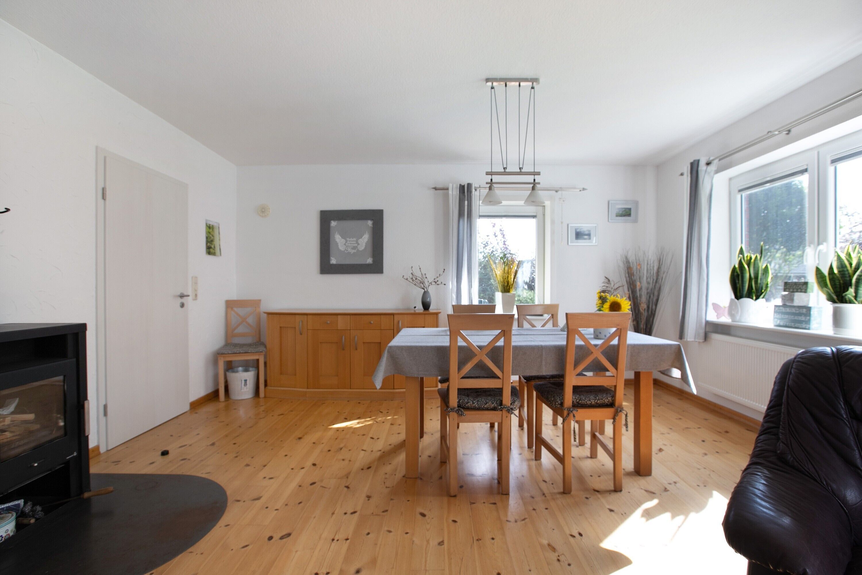 Un coin repas avec une table et des chaises en bois, une cheminée et une fenêtre agrémentée de plantes.