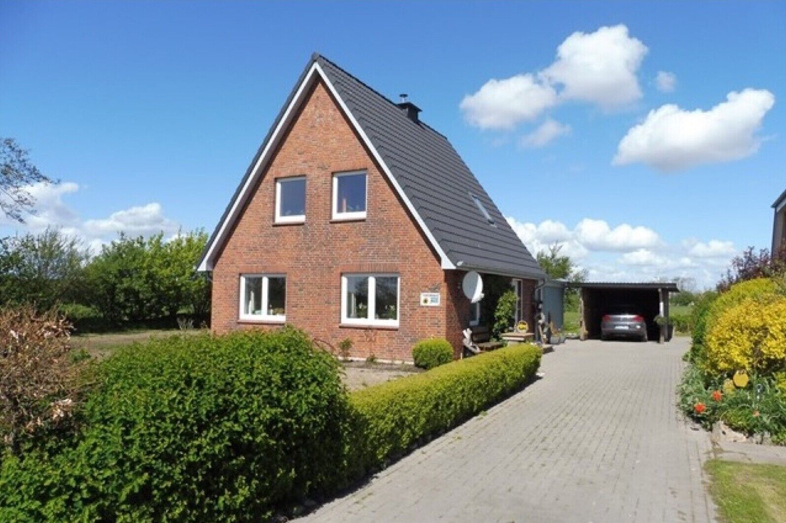 Une maison à deux étages, construite en briques, avec un toit en pente, une allée couverte et un garage.