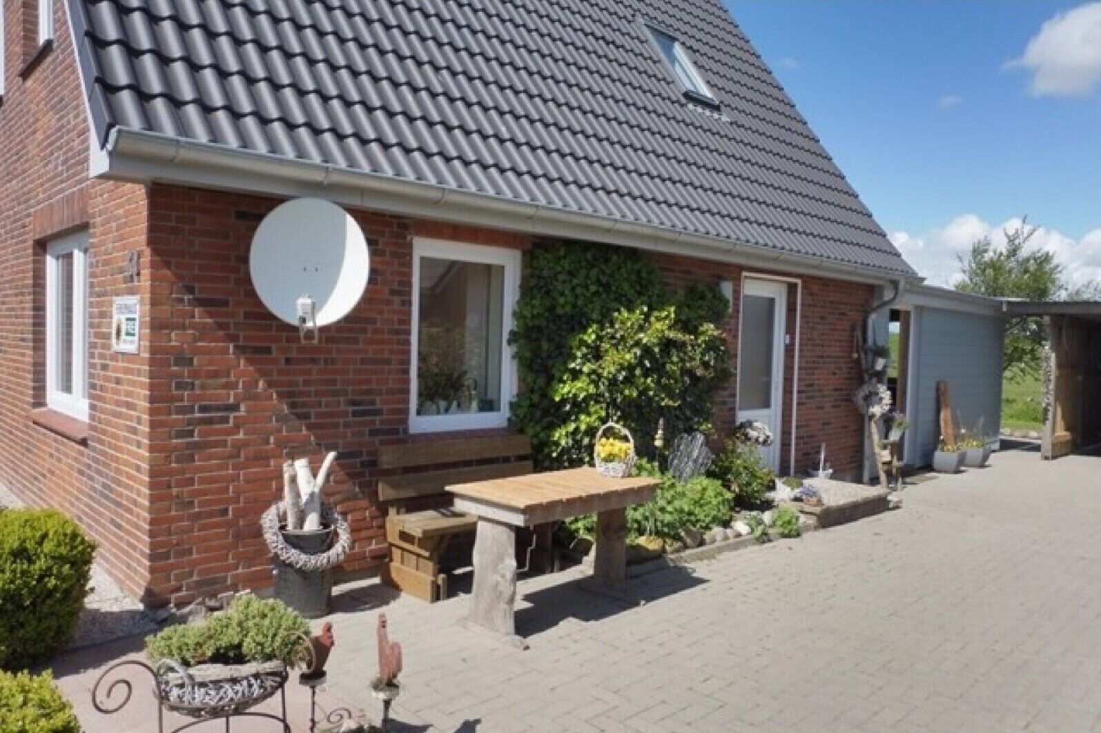 A brick house with a tiled roof, a satellite dish, a wooden bench, and a garden with potted plants.