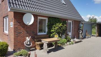 A brick house with a tiled roof, a satellite dish, a wooden bench, and a garden with potted plants.