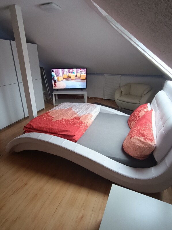 A modern bedroom with a curved bed, a television, a chair, and a wardrobe.