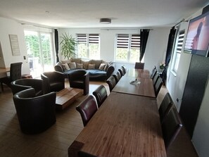 A modern living room with a long wooden dining table, leather sofas, and a large potted plant.