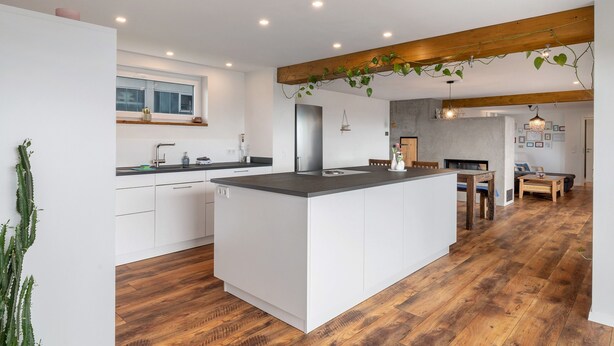 Une cuisine moderne avec des meubles blancs, un îlot central, un plancher en bois et un coin repas comprenant une table et des chaises.