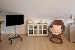 A room with a television on a stand, a wicker chair, a cabinet with glass doors, and a lamp.