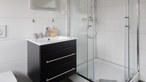 A modern bathroom with a glass shower enclosure, a white sink, and a black vanity.