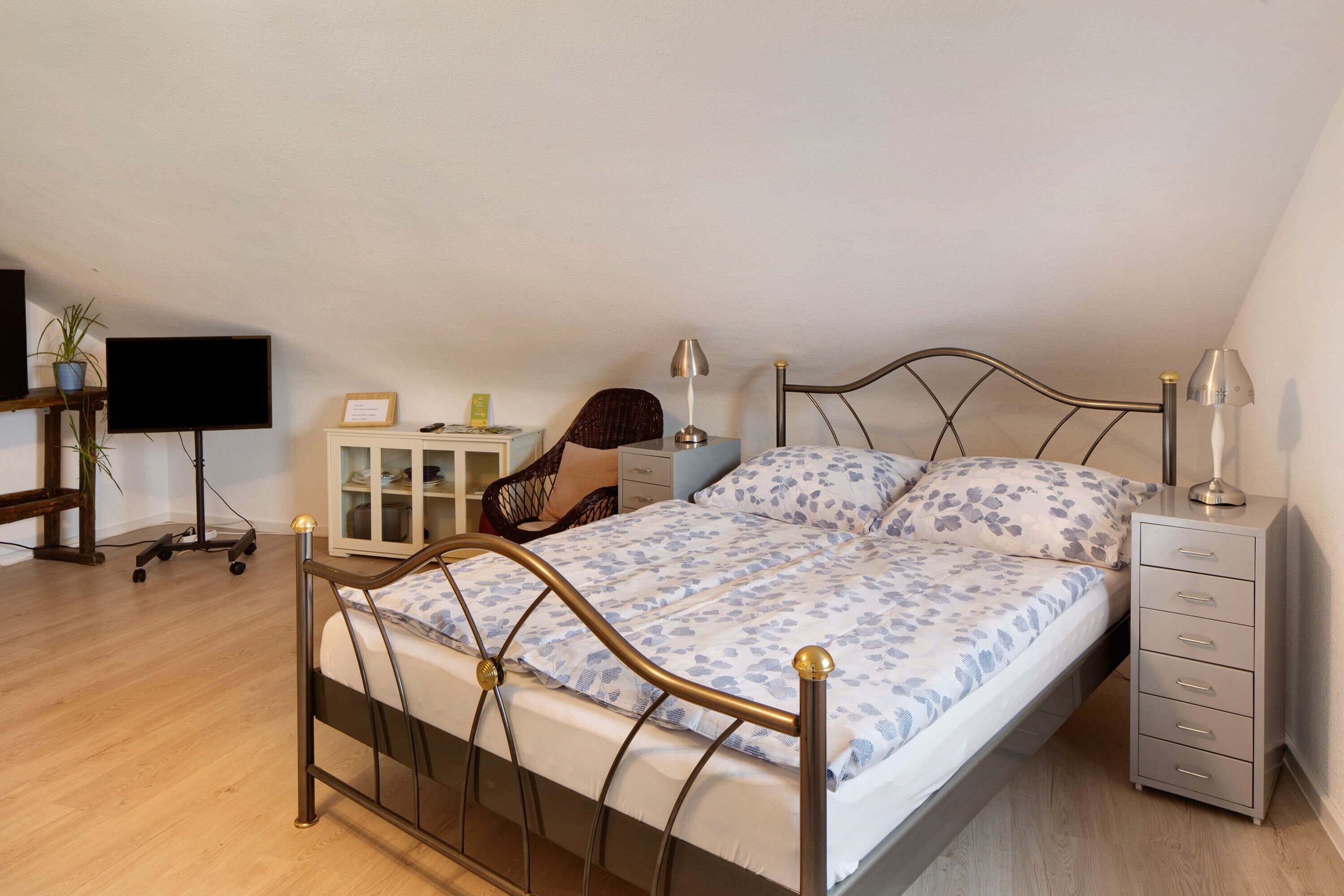 A bedroom with a bed, bedside tables, a desk, a chair, and a television.