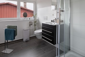 A modern bathroom with a glass shower enclosure, a white toilet, a black vanity, and a towel rack with a green towel.
