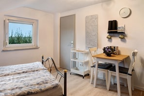 A bedroom with a bed, a desk, a chair, a shelf with items, and a window with a view.