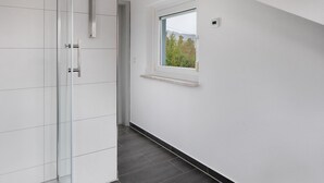 A modern bathroom with a glass shower enclosure, a small window with a view, and a white tiled floor.