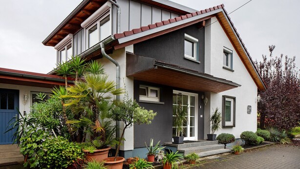 A modern two-story house with a sloped roof, a front porch, and a variety of potted plants.