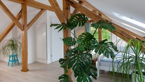 A room with a sloped ceiling, wooden beams, a bed, and large green plants.