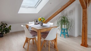 A dining area with a wooden table, white chairs, a vase with sunflowers, and a skylight.