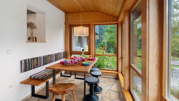 A wooden ceiling, a table with colorful bowls, a bench, and a view of greenery outside.