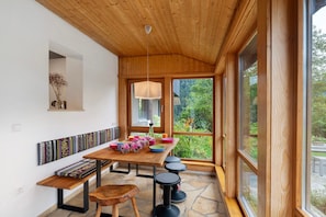 Techo de madera, una mesa con cuencos de colores, un banco y vistas al verdor exterior.