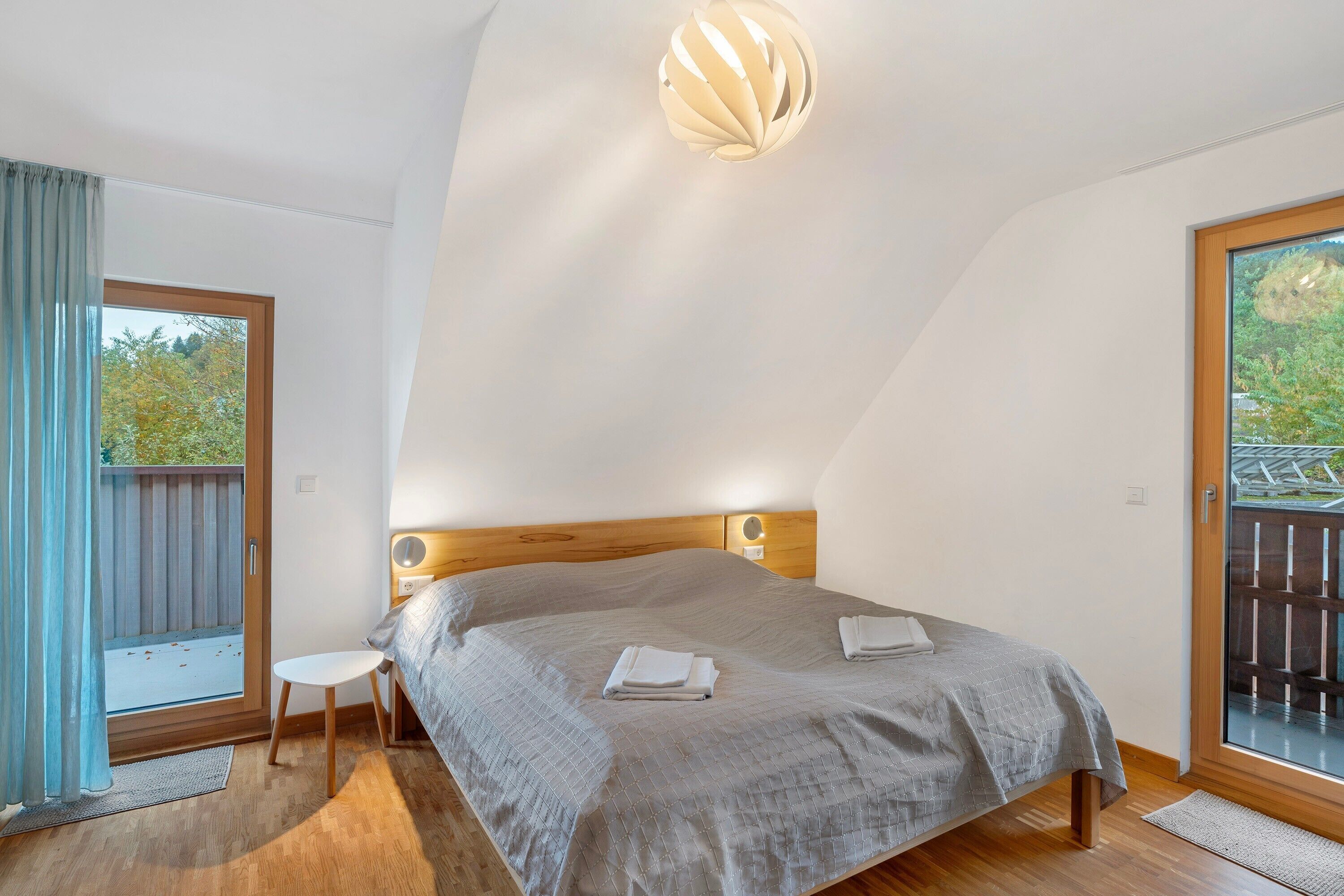 Ein Schlafzimmer mit einem Bett, einem kleinen Nachttisch, einem Fenster mit Vorhängen und einer Deckenleuchte.