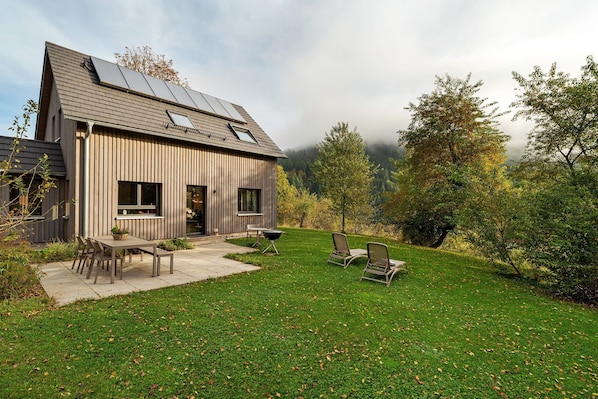Una casa moderna con techo inclinado, paneles solares, un patio con mobiliario exterior y un césped bien cuidado.