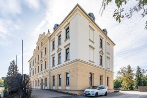 A multi-story building with a symmetrical facade, large windows, and a paved entrance area.