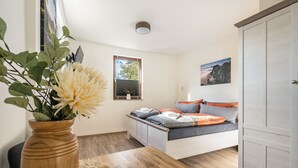Ein Schlafzimmer mit Bett, einem Holztisch mit Vase, einem Fenster mit Jalousien und einer Tür.