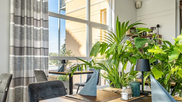 Ein Essbereich mit Tisch für zwei Personen, Stühlen, einer Topfpflanze, einer Lampe und Blick ins Freie.