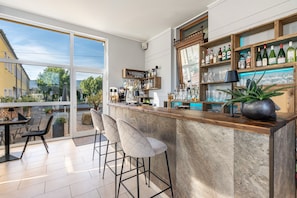 A modern bar area with a large window, bar stools, and shelves of bottles.
