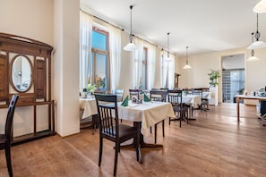A dining area with wooden tables and chairs, large windows, and hanging pendant lights.