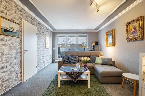 A living room with a sofa, coffee table, and a view through large windows.
