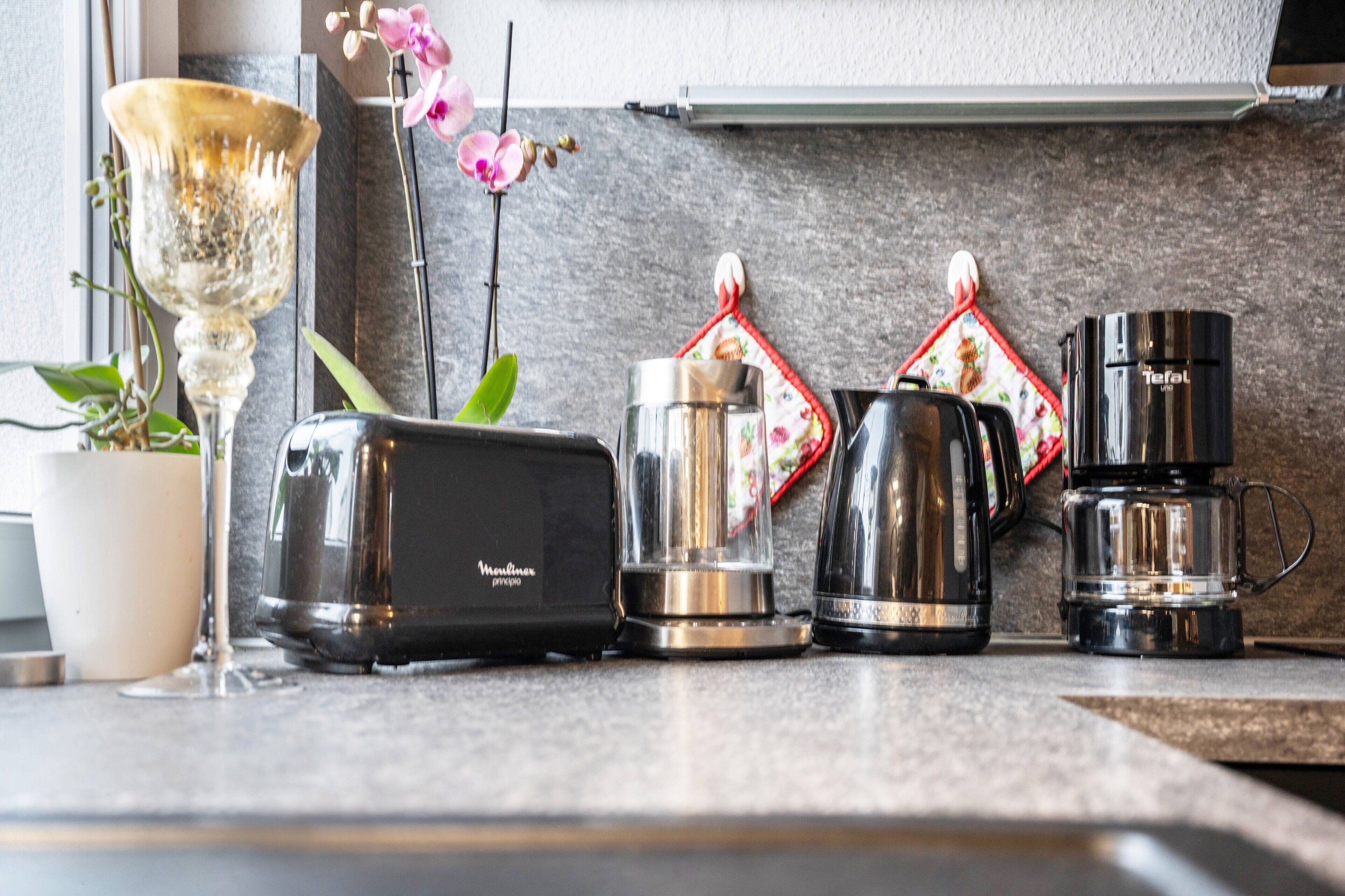 Een aanrecht met een broodrooster, een blender, een koffiezetapparaat en een decoratieve vaas met bloemen.