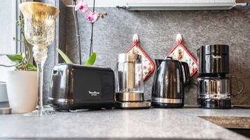 Een aanrecht met een broodrooster, een blender, een koffiezetapparaat en een decoratieve vaas met bloemen.