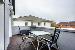 Ein Balkon mit Tisch und Stühlen, Blick auf ein Gebäude mit Ziegeldach, und klarer Himmel.