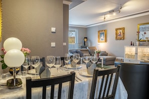 A dining area with a table set for six, chairs, a chandelier, and a view of the living room.